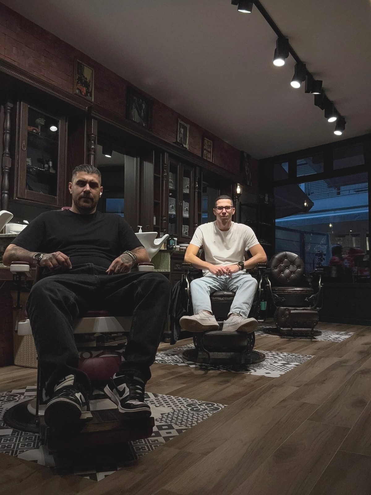 Οι δύο barbers του Barberians καθισμένοι στις vintage δερμάτινες καρέκλες του κουρείου, στη Ναβαρίνου