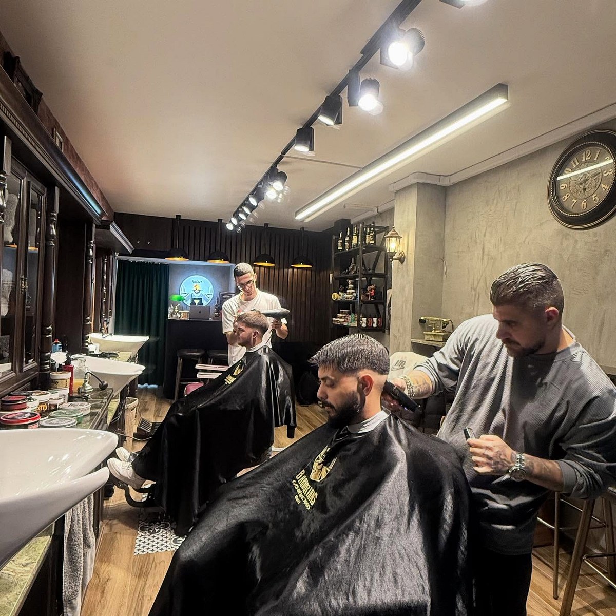 Το κουρείο Barberians στη Ναβαρίνου εν ώρα δράσης: δύο barbers δουλεύουν ταυτόχρονα, ξύλινα ντουλάπια, το neon με τον βασιλιά